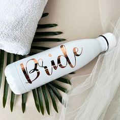 a white bottle with the word bride on it next to some palm leaves and a towel