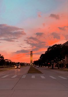 the sun is setting over a street with cars driving on it and trees in the background