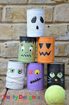 a stack of tin cans with faces painted on them and a tennis ball sitting next to it