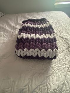 a crocheted bag sitting on top of a white bed covered in blankets and pillows