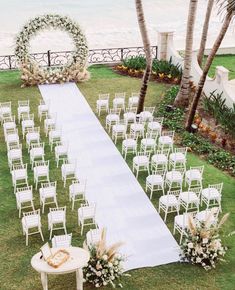 an outdoor ceremony setup with white chairs and flowers on the grass near the beach, surrounded by palm trees