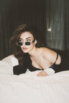 a woman wearing sunglasses laying on top of a bed