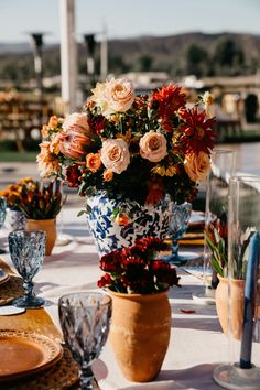 an arrangement of flowers in vases on a table with plates and utensils