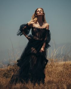 a woman wearing a black dress standing in tall grass