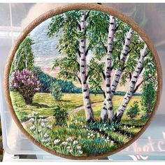 a painting is hanging on the wall in front of a glass case with trees and flowers painted on it