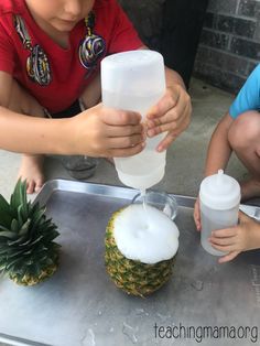 two young children are filling their cups with water and pineapples on the table