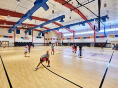 people are playing basketball in an indoor gym with wood floors and blue beams on the ceiling