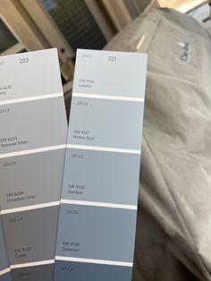 two gray paint samples sitting next to each other on top of a table in front of a bed