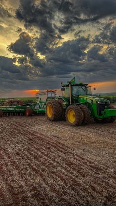 a green tractor is driving in the middle of a field with other farm equipment on it