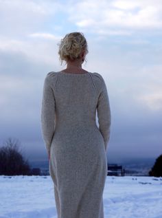 a woman is standing in the snow wearing a long cardigan and looking out into the distance