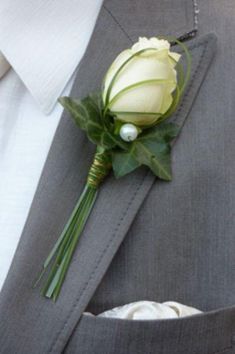 a boutonniere with a white rose and greenery on the lapel