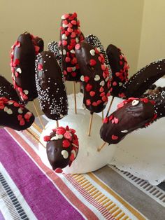 chocolate covered strawberries are arranged on sticks in a white vase with red and white sprinkles