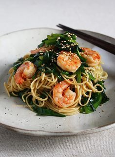 a white plate topped with pasta and shrimp next to chopsticks on a table