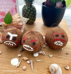 three coconut balls with painted faces on them sitting on a table next to sea shells