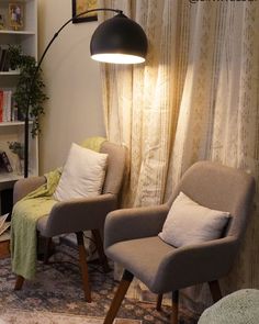 A cozy reading nook featuring two modern chairs with light cushions, a floor lamp with a large dome shade, and a bookshelf filled with numerous books. A white floor lamp arches over the setup, and sheer curtains drape softly in the background, enhancing the warm, inviting ambiance of the space. Faux Black Marble, Cozy Lamp, Arch Floor Lamp, Fall Movie, Black Arch, Windmill Decor, Arc Floor Lamp, Arched Floor Lamp, Perfect Night