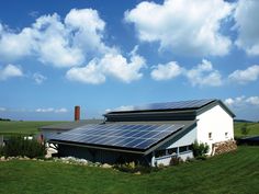 a house with solar panels on the roof in a green field under a cloudy blue sky