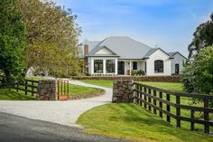 a white house with a black fence in the front yard and trees on both sides