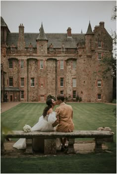 a bride and groom sitting on a bench in front of an old castle like building