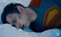 a man laying in the snow with his head on his chest and eyes closed, wearing a superman t - shirt