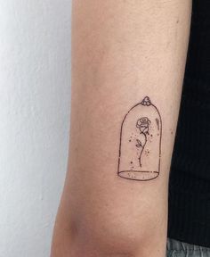 a woman's arm with a small tattoo of a rose in a glass jar