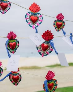 hearts and flowers are hanging on a line by the beach with cards attached to them