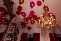 red and gold balloons are hanging from the ceiling in a room with white trimmings