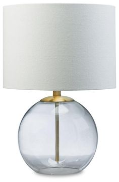 a clear glass lamp with a white shade on the bottom and a gold metal base