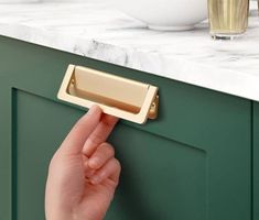 a person's hand is holding the handle on a green cabinet door with marble countertops