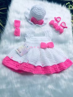 a crocheted baby dress and hat with pink trimmings on white fur