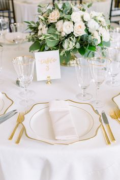 the table is set with white flowers and gold place settings for an elegant dinner party