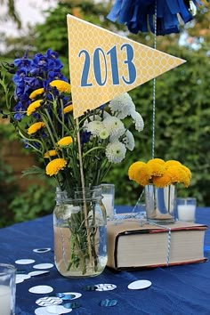 a table topped with vases filled with yellow and white flowers next to an open book