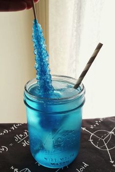 a hand holding a toothbrush in a blue mason jar with writing on the table