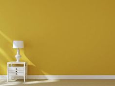 an empty room with yellow walls and a white dresser in the corner, next to a lamp