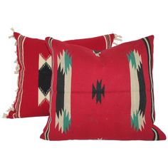 two red pillows with black, white and green designs on the front one has tassels