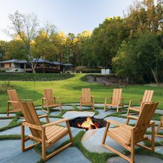 a fire pit surrounded by lawn chairs in the middle of a yard with trees and grass