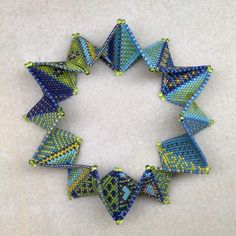 a close up of a bracelet made with blue and green bead squares on a white surface