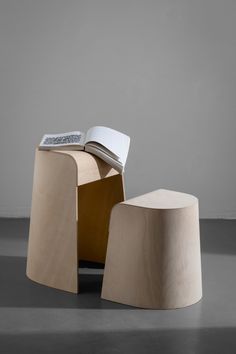 two wooden stools sitting next to each other on top of a gray floor with a book in the middle