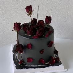 there is a black cake with red flowers on the top and bottom, sitting on a white table