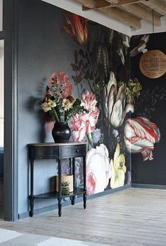 a room with flowers painted on the wall and a vase full of flowers in front of it