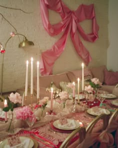 the table is set with pink and white flowers, candles, and china plates on it