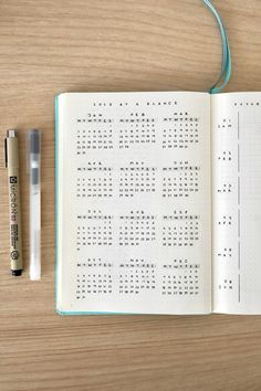 an open notebook and pen sitting on top of a wooden table next to each other