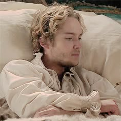 a man laying on top of a bed next to a white blanket and pillow with his eyes closed