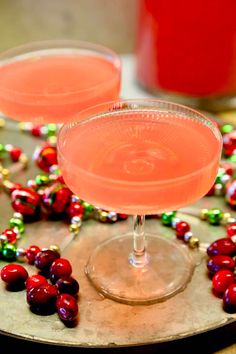 two glasses filled with pink and red drinks on top of a silver platter next to christmas decorations