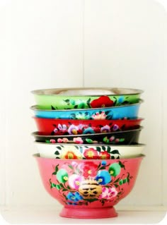 four bowls are stacked on top of each other in different colors and designs, with flowers painted all over them