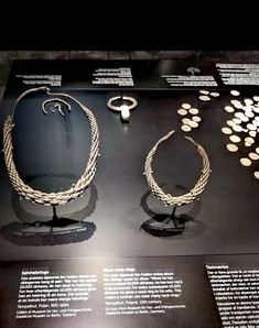 two necklaces on display in a museum case with other jewelry items around them and information about their origin