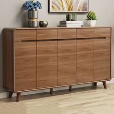 a wooden sideboard with two vases on top of it next to a painting