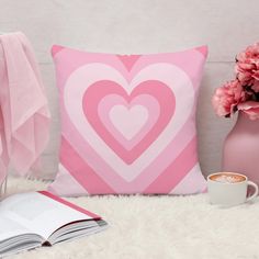 a pink heart pillow sitting on top of a bed next to a cup of coffee