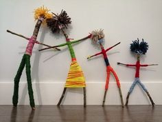 three small children made out of sticks and yarn standing in front of a white wall