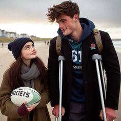 a man and woman standing on the beach with crutches holding a rugby ball