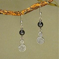 three black and silver earrings hanging from a branch with a twig in the background